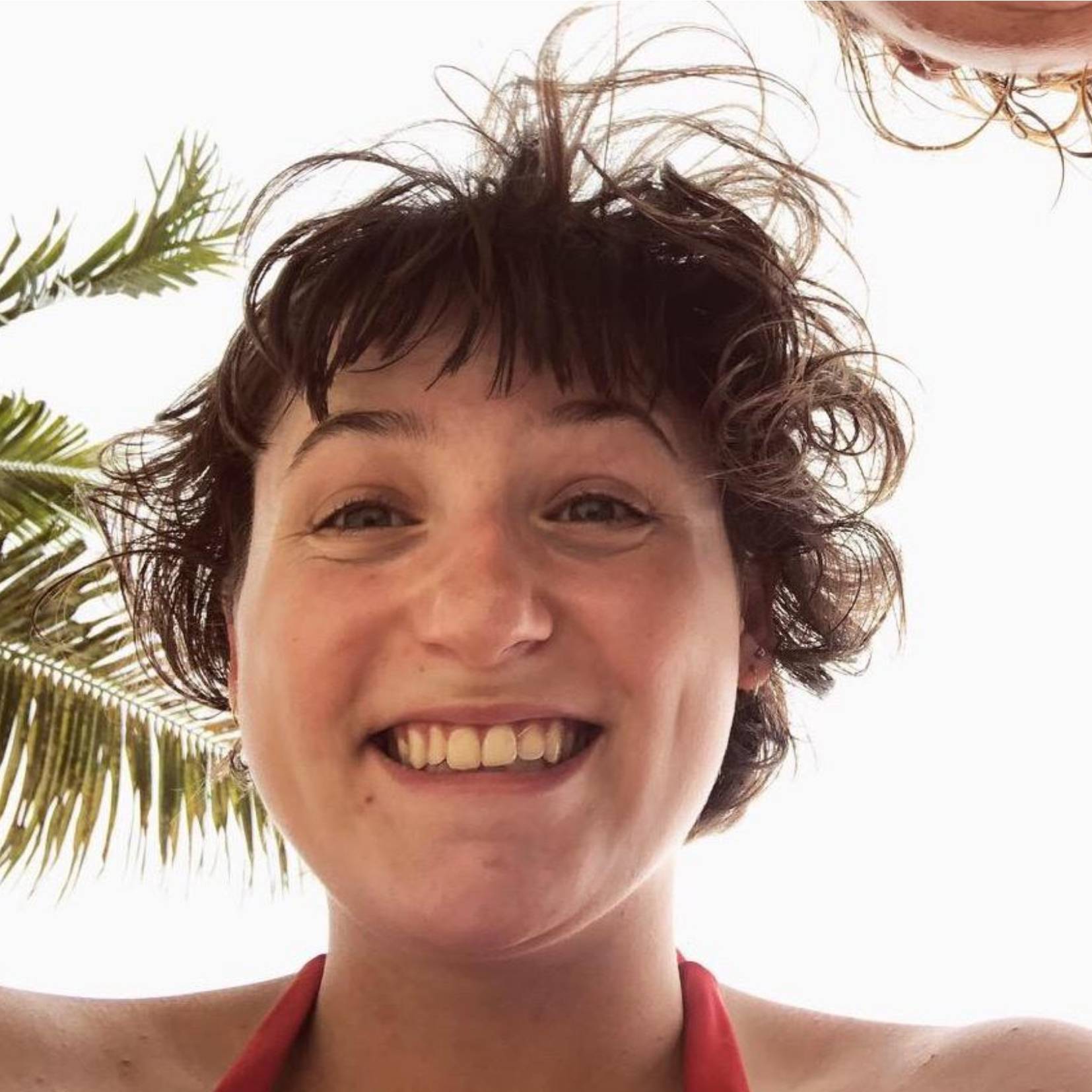 Smiling girl looking down at camera with palm trees in back